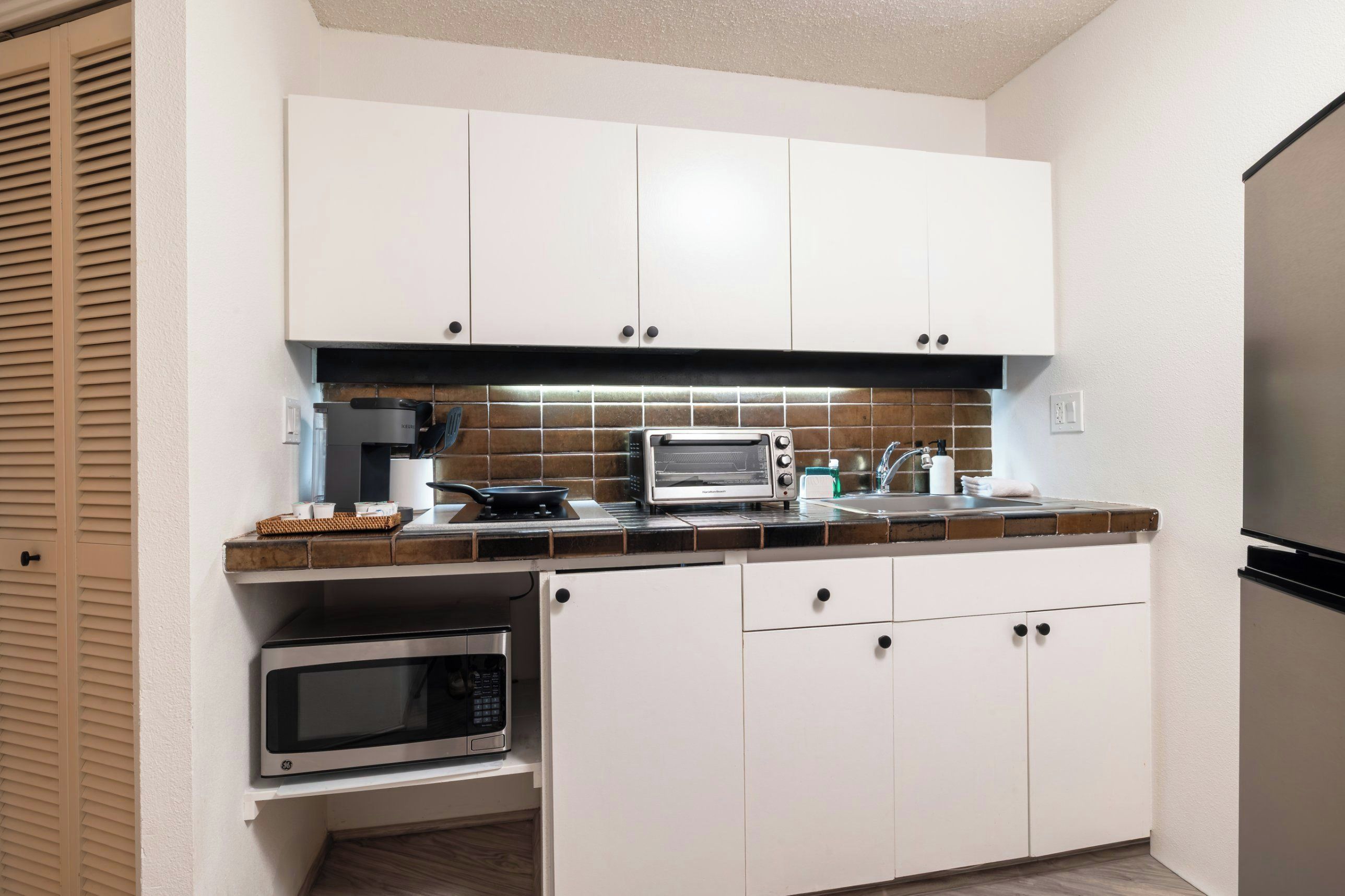 A compact kitchen with white cabinets, a microwave, a kettle, and a toaster.
