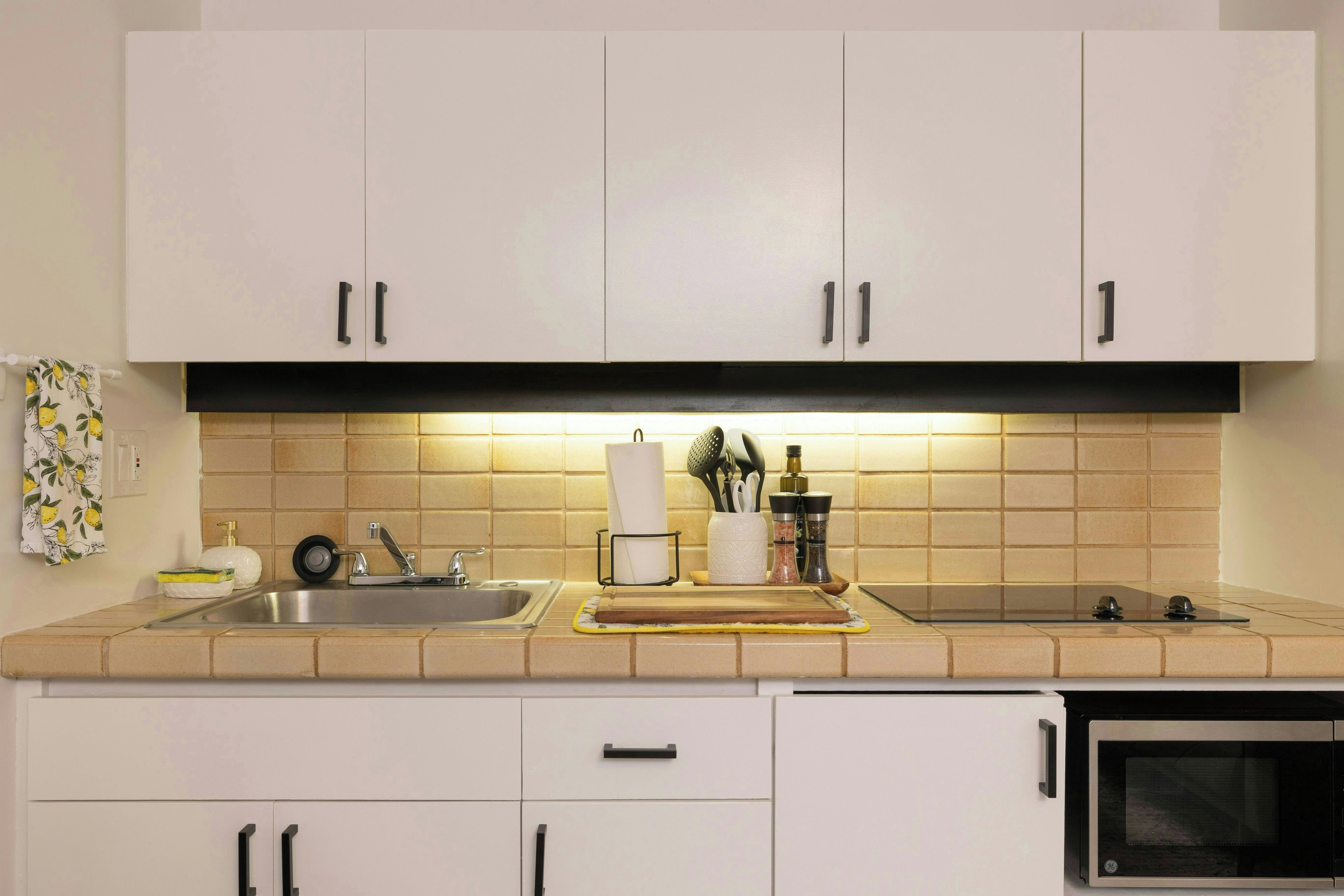 A kitchen with white cabinets, a stainless steel sink, and a microwave.