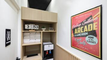 Habitación de hotel con estante empotrado que contiene toallas dobladas, un reloj y un cartel de Wi-Fi. Se observa un cartel enmarcado que anuncia una sala de juegos.