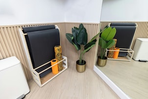 A modern room with a bed, a small white bedside table, a mirror, and two potted plants.