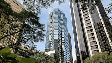 A modern high-rise building with a glass facade, surrounded by lush green trees.