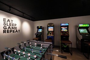 A room with a foosball table, two arcade games, and a wall with the phrase 'EAT SLEEP GAME REPEAT'. - Bishop Suites Downtown Honolulu (Honolulu)