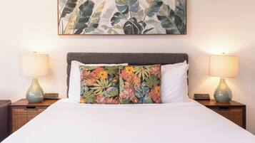 A hotel room with a bed, two nightstands, two lamps, a floral artwork above the bed, and a power strip on each nightstand.