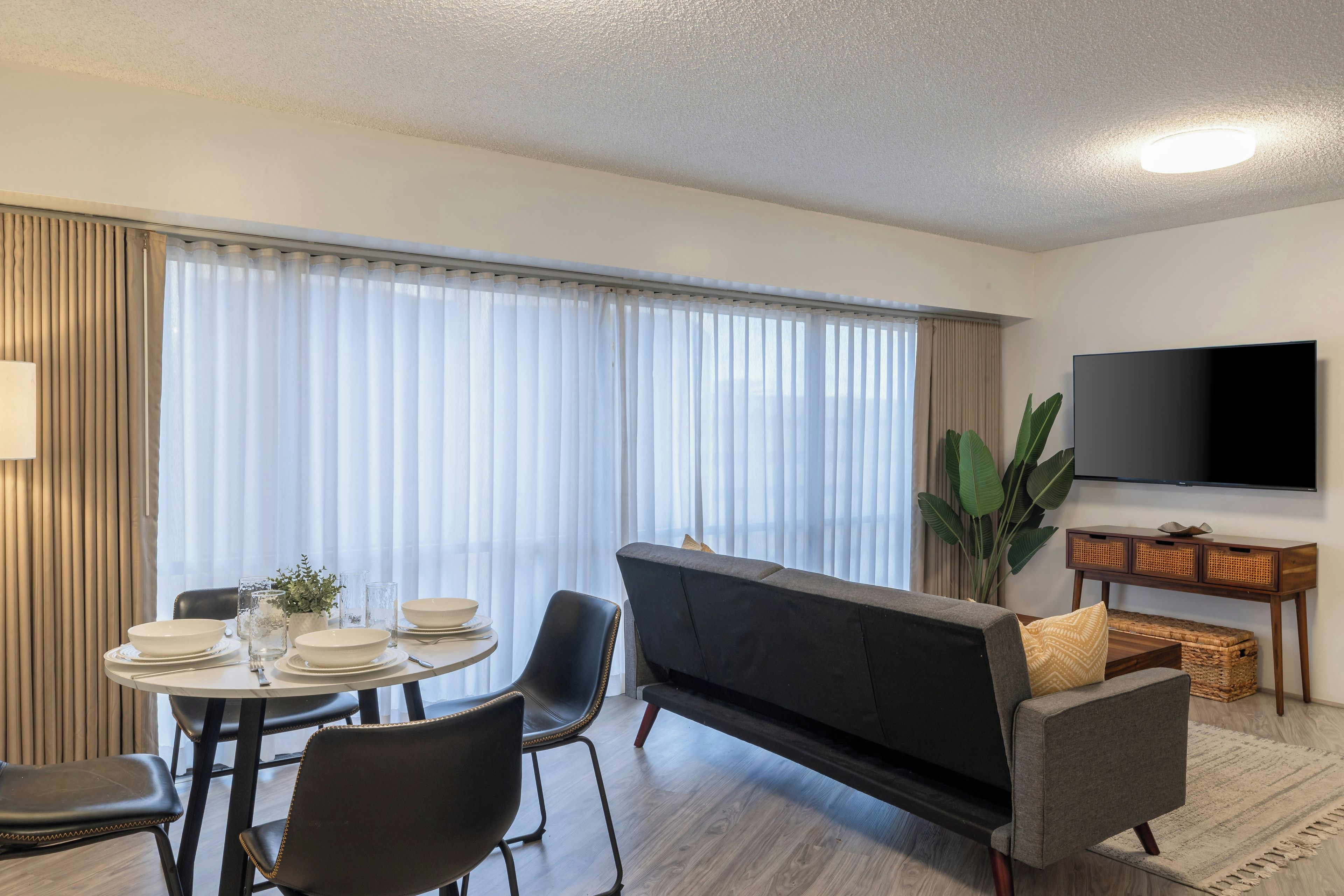 Un salon moderne comprenant un canapé, une table à manger, des chaises, un téléviseur à écran plat et une grande fenêtre avec des rideaux.