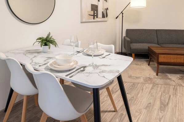 A dining area with a marble table, white chairs, and a grey sofa.