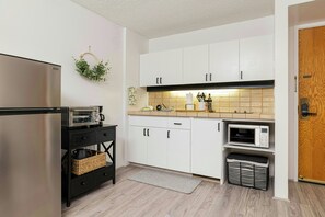 A compact kitchen with white cabinets, a stainless steel refrigerator, a microwave, and a toaster. - Bishop Suites Downtown Honolulu (Honolulu)