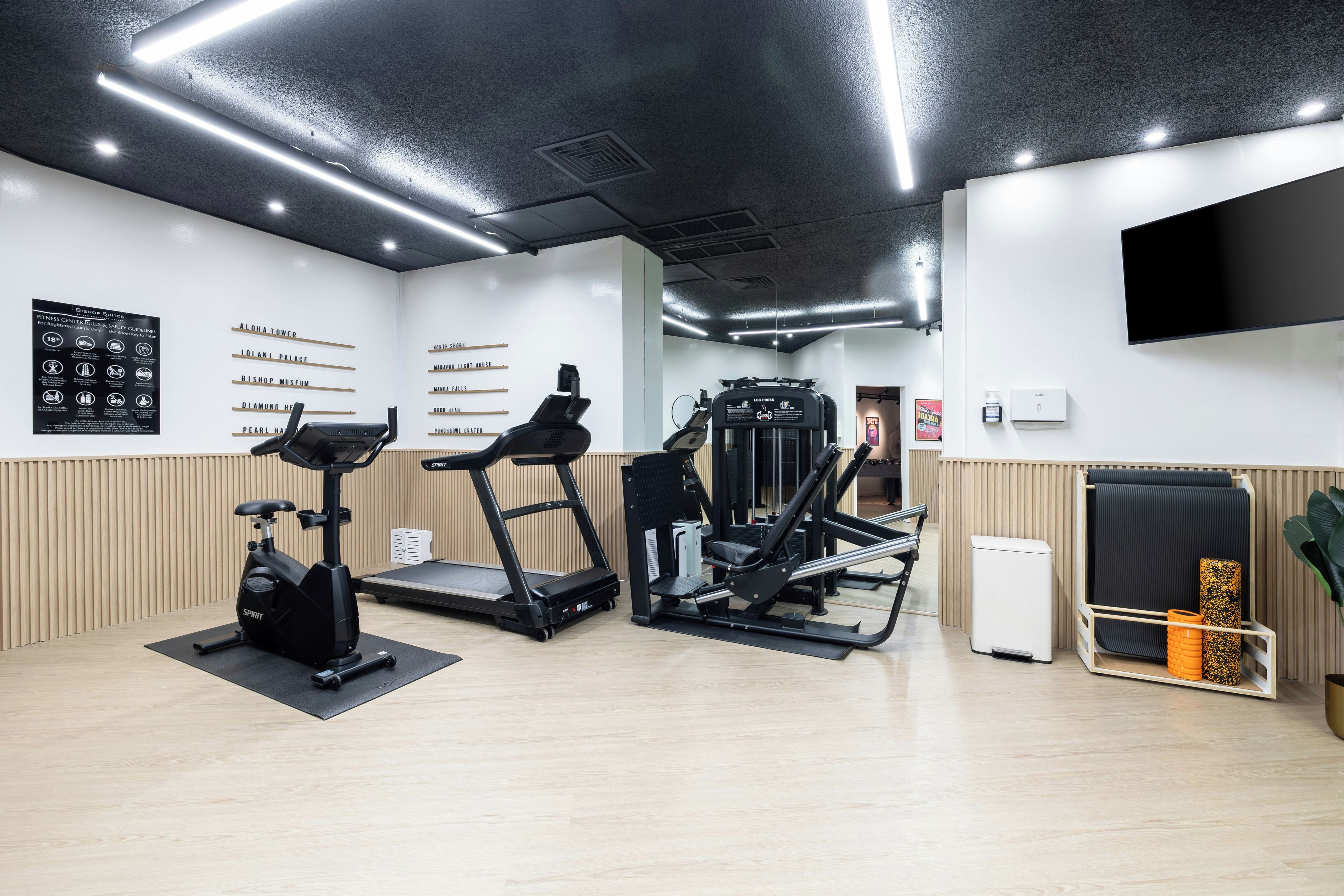 Una palestra con tapis roulant, macchinari per pesi e una parete con i nomi delle aree dedicate all'allenamento.