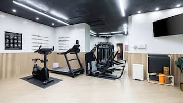 Una palestra con tapis roulant, macchinari per pesi e una parete con i nomi delle aree dedicate all'allenamento.