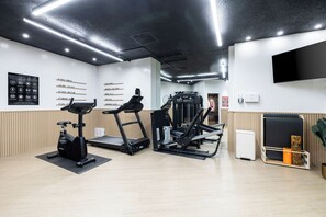 Ein Fitnessstudio mit Laufbändern, einem Kraftgerät und einer Wand mit Beschriftungen für verschiedene Trainingsbereiche.