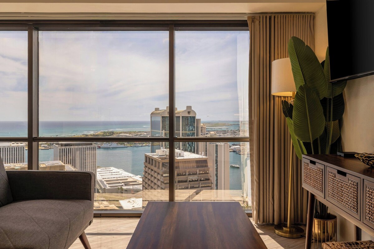 A hotel room with a large window offering a view of the city skyline and a body of water.