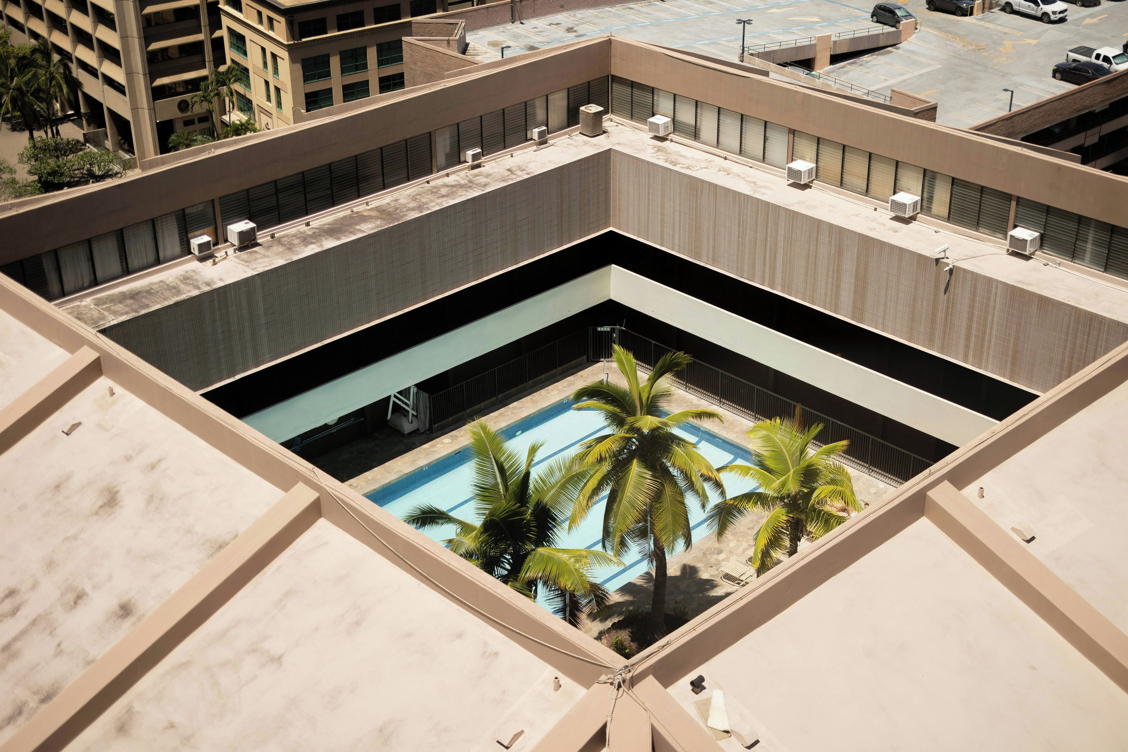 A rooftop pool with palm trees, surrounded by a building with multiple air conditioning units.