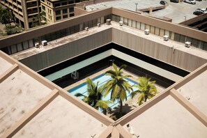 A rooftop pool with palm trees, surrounded by a building with multiple air conditioning units. - Bishop Suites Downtown Honolulu (Honolulu)