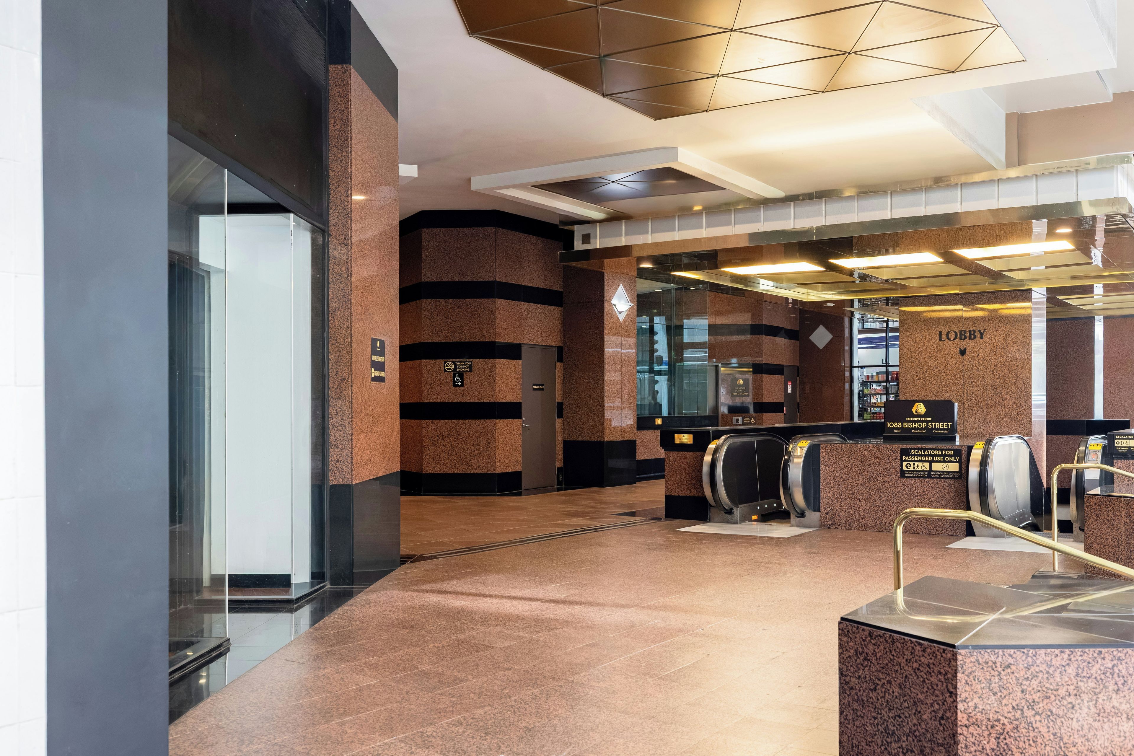 A modern elevator area with a marble floor, a glass elevator door, and a sign indicating 'Lobby'.