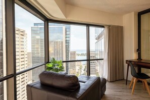 A modern room with a leather sofa, a dining table with chairs, and large windows offering a city view. - Bishop Suites Downtown Honolulu (Honolulu)