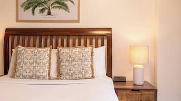 A neatly made bed with patterned pillows, a wooden headboard, a bedside lamp, and a framed botanical illustration on the wall.