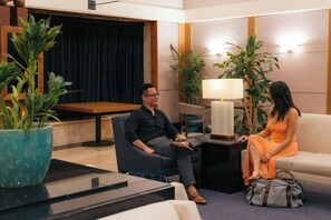 A hotel lobby with a seating area, a table with a lamp, and a potted plant.