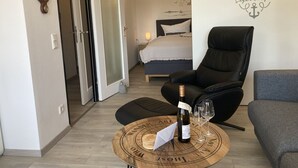A modern hotel room with a bed, a lounge chair, a small table with a bottle and glasses, and a wall with nautical-themed decor.