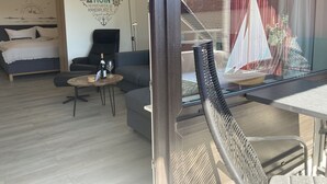 A modern living room with a bed, a sofa, a small round table with a bottle and glass, and a wall with nautical-themed decor.