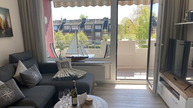 A modern living room with a grey sofa, a round coffee table with a compass design, and a view of a sailboat through a window.