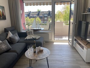 Een moderne woonkamer met een grijze bank, een ronde salontafel met een kompasprint en uitzicht op een zeilboot door een raam.
