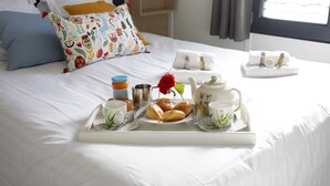 A neatly made bed with a tray of breakfast items including croissants, a red rose, and tea set.