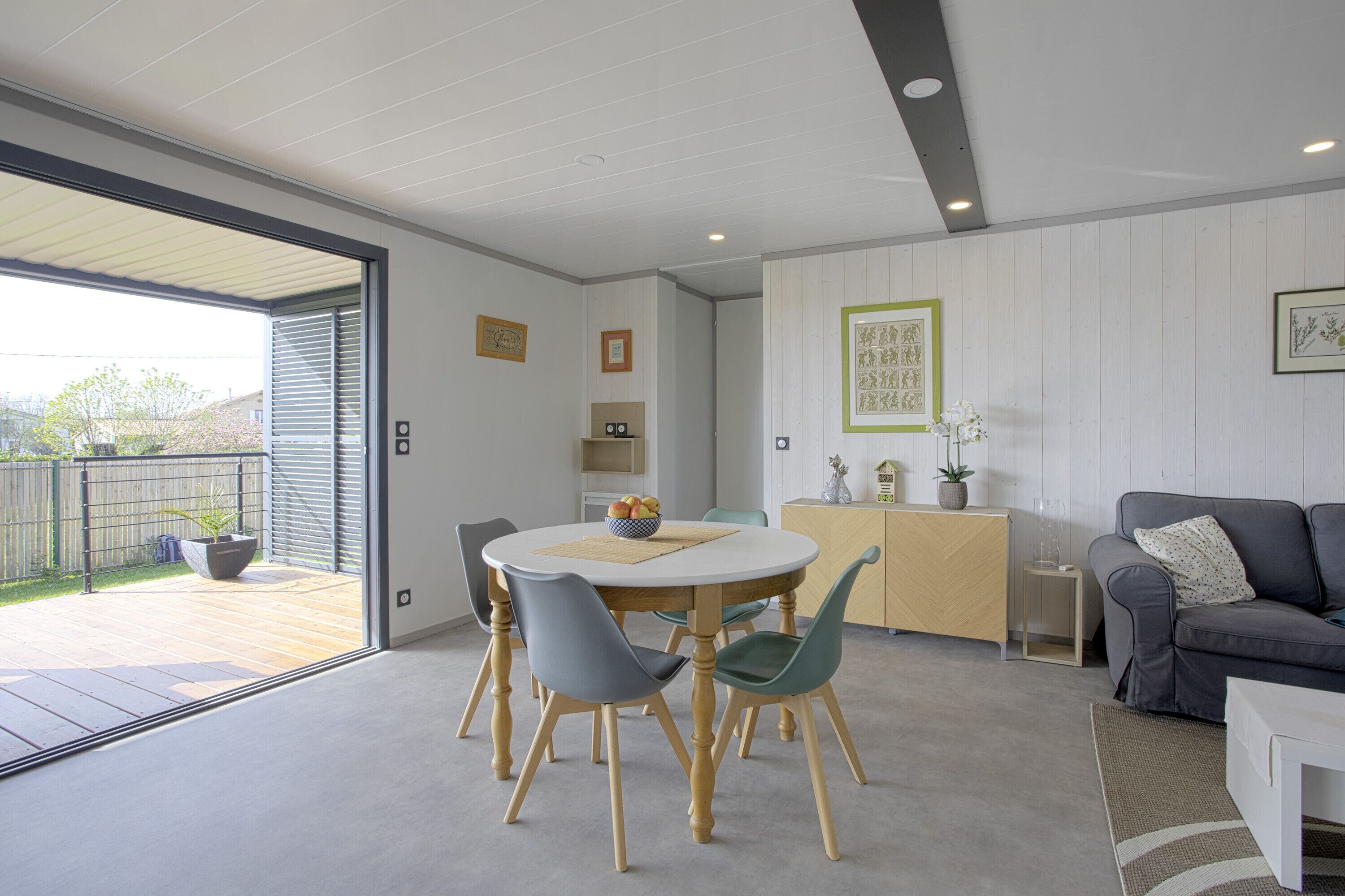 Een moderne woonkamer met een eethoek, met een ronde tafel, stoelen, een grijze bank en een klein kastje.