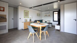 A modern living room with a round wooden dining table, two blue chairs, a sofa, and a TV.
