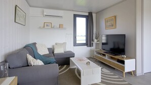 A modern living room with a grey sofa, a white coffee table, and a flat-screen TV on a wooden stand.