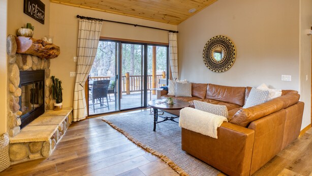 A cozy living room with a stone fireplace, leather sofa, and a large sliding glass door leading to a deck. - Torreon Cardinal Landing Cabin With Party Garage (Show Low)