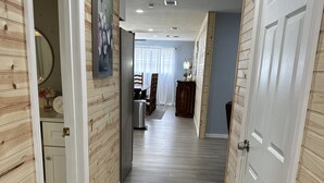 A hallway with wooden paneling, a dining area with a table and chairs, and a kitchen area with cabinets and a sink.