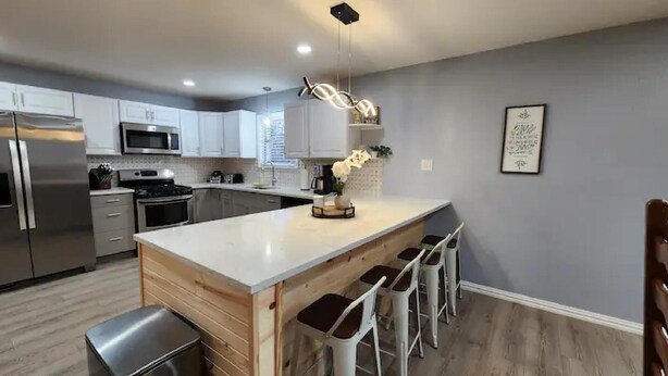 A modern kitchen with a central island, bar stools, stainless steel appliances, and a pendant light.