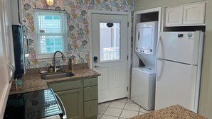 A compact kitchen with a sink, countertop, cabinets, a refrigerator, and a door leading to a balcony. - Happiness Comes in Waves 🌊Steps to the Gulf 👣Free Parking (Gulf Shores)