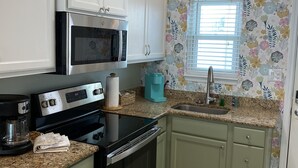 A kitchen with white cabinets, a microwave, an oven, a coffee maker, and a window with blinds.