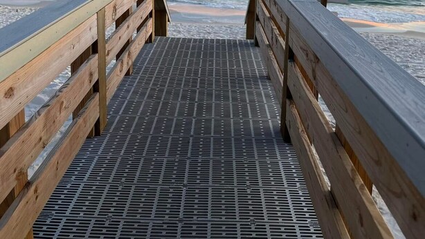A wooden pier leading to the ocean with a metal grate floor.