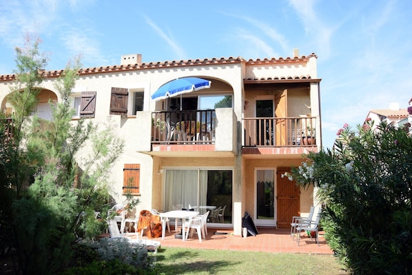 A two-story building with a balcony, a patio with outdoor furniture, and a garage.