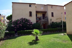 Un edificio a due piani con un balcone, un piccolo giardino con fiori rosa e una palma.