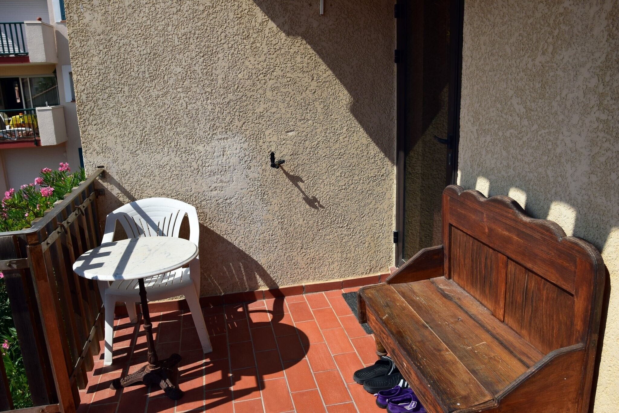 A balcony with a white plastic chair, a wooden bench, and a scooter.