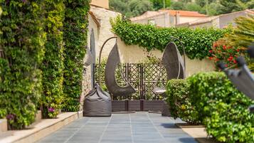 Eine Terrasse mit zwei Korbstühlen, einem kleinen Tisch und einer Wand mit Pflanzenzier.
