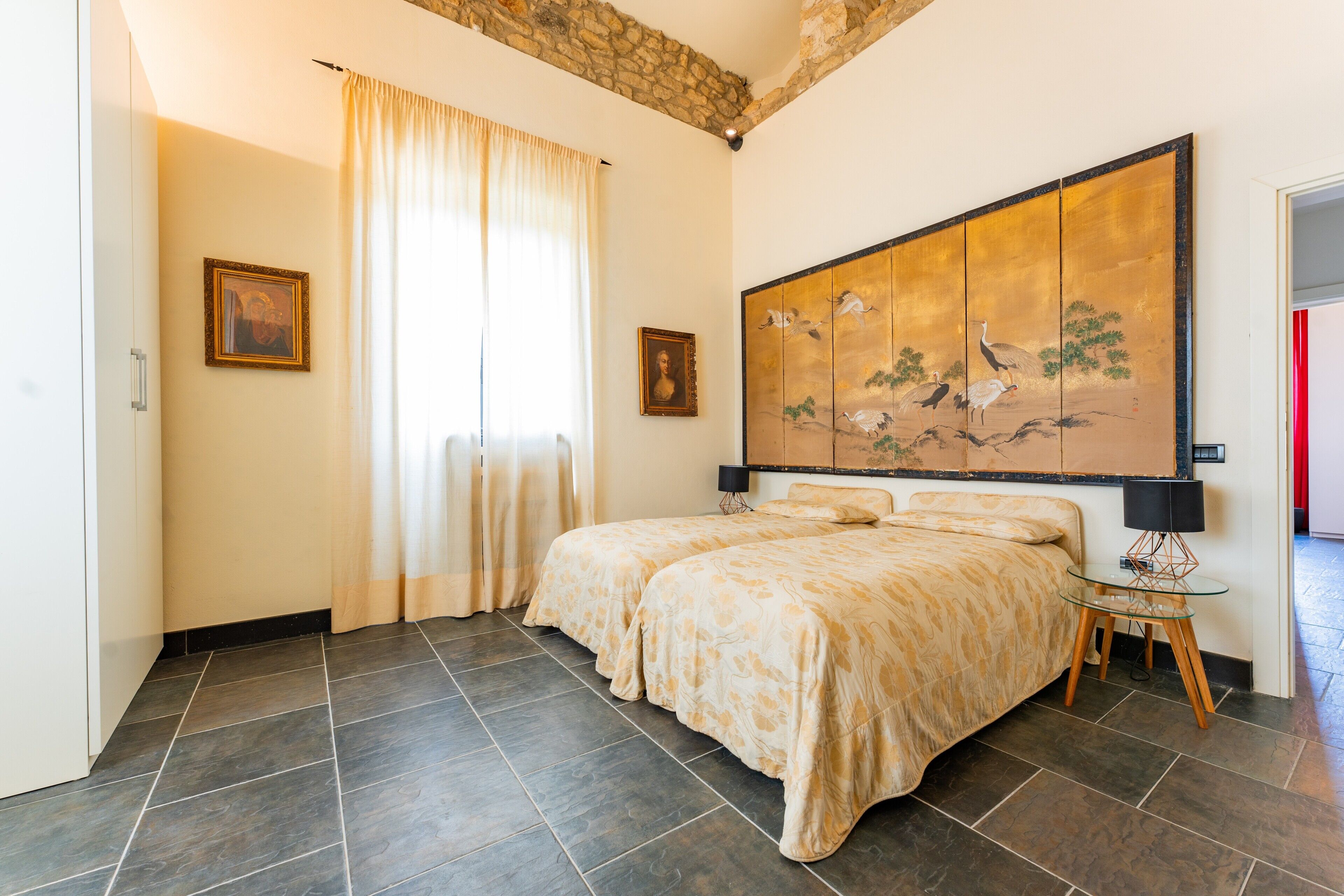 Une chambre avec un grand lit, un tableau au mur et une fenêtre avec des rideaux.
