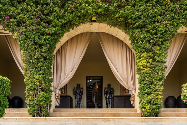 An arched entrance with draped curtains, statues, and a staircase leading up.