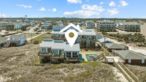 A coastal residential area with modern houses, a swimming pool, and a beach in the background. - 5381- Sol-T-Escape - Wake to Ocean Views | Oceanfront KDH Condo (Kill Devil Hills)