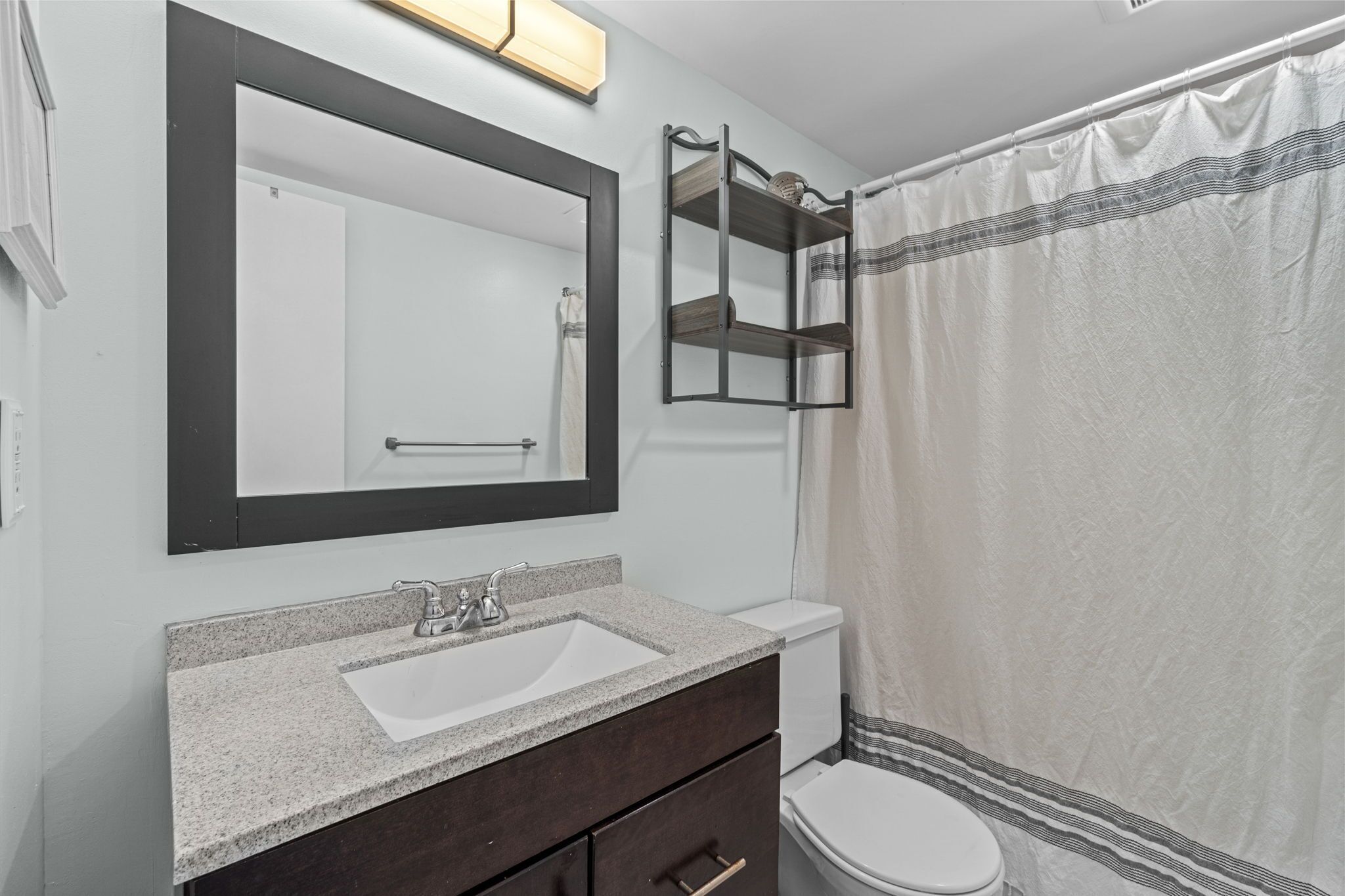 A bathroom with a white sink, dark vanity, a large mirror, and a shower curtain.