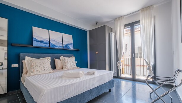 Una habitación de hotel moderna con una cama grande, una pared azul decorativa, un balcón con vistas y un diseño minimalista.
