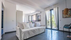 Una sala moderna con un sofá, una silla, un ventanal grande y una puerta que da a otra habitación.