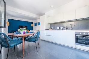 A modern kitchen with white cabinets, a built-in oven, and a dining area with a wooden table and blue chairs. - Holiday Home 'Ninai Sea Holiday Apartment' with Balcony, Wi-Fi and Air Conditioning (Furci)