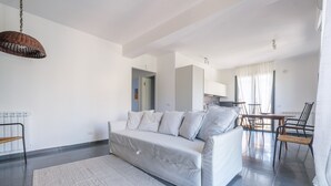 A modern living room with a sofa, a dining area with chairs, and a kitchen in the background.