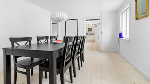 A dining area with a black table and chairs, a hanging light fixture, and a view into the kitchen. - Amazing apartment in Tisvildeleje (Tisvildeleje)