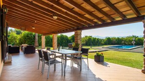 Een terras buiten met een houten pergola, een zwembad en een verzorgd gazon.