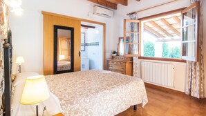 Een slaapkamer met een bed, een dressoir, een raam met gordijnen, een radiator en een airconditioning.