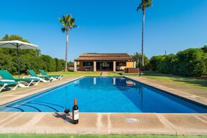 A swimming pool with lounge chairs, a building with a tiled roof, and palm trees.